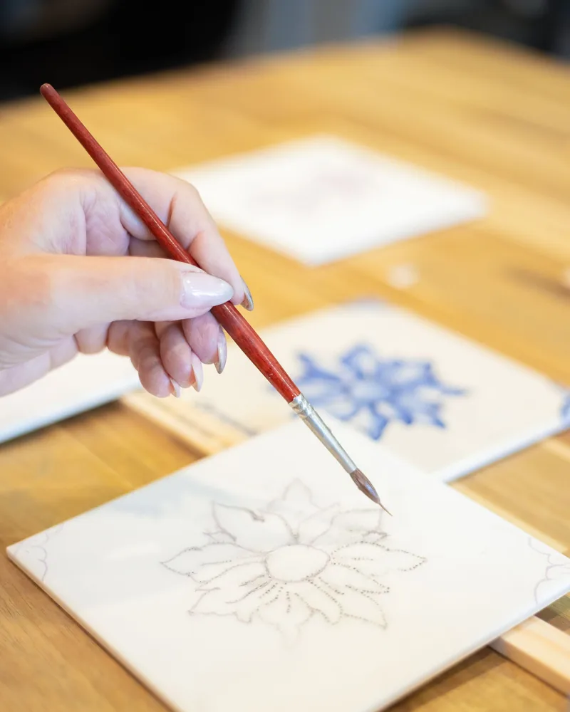 Pincel fino aplicando color sobre un azulejo blanco con el dibujo floral pasado a estarcido